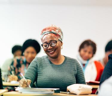 A woman in a classroom taking notes, surrounded my several other students