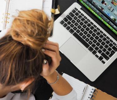 Woman with hands on head in stress looking at a laptop
