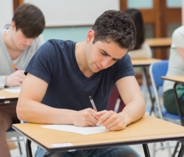 Students writing on an exam desk