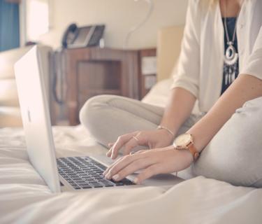 woman typing on laptop on bed