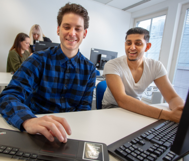 Two male students sitting at laptops in a classroom