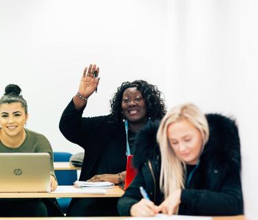 Three students participating and taking notes in a classroom