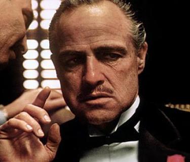 Man whispering to another man sitting down wearing a tuxedo