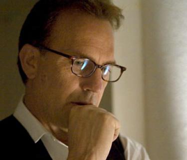 Man with glasses holding hand near mouth, thinking deeply
