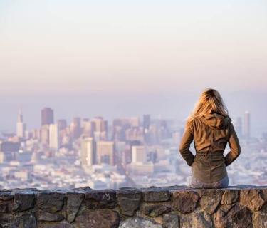 Woman sits on stone wall overlooking a large city landscape