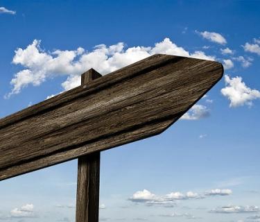 Wooden, blank sign post against a blue sky with clouds