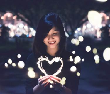 A woman with dark hair looking down at a light shaped like a heart with other lights around her