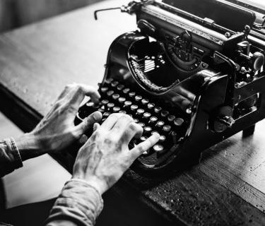 Black and white photo of a pair of hands typing on a typewriter