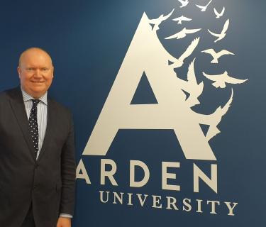 Man stood next to Arden University logo