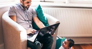 Man studying on a laptop while looking after a baby 